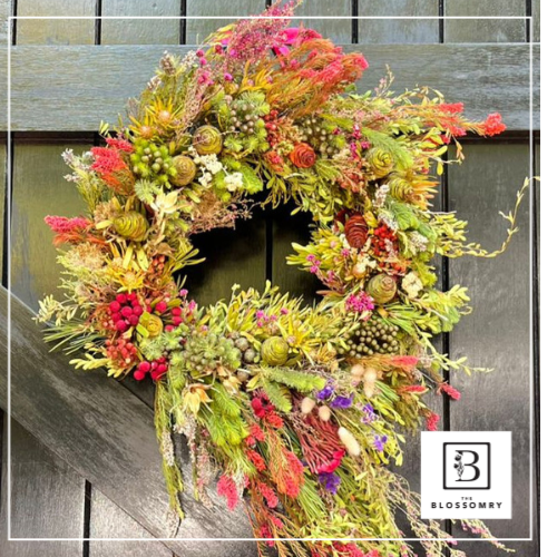 Handcrafted Christmas wreath made with pine, berries, and festive ribbon hanging on a wooden door.